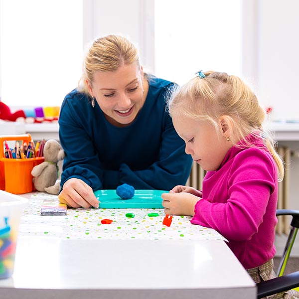 an adult female playing with a young girl using play-doh