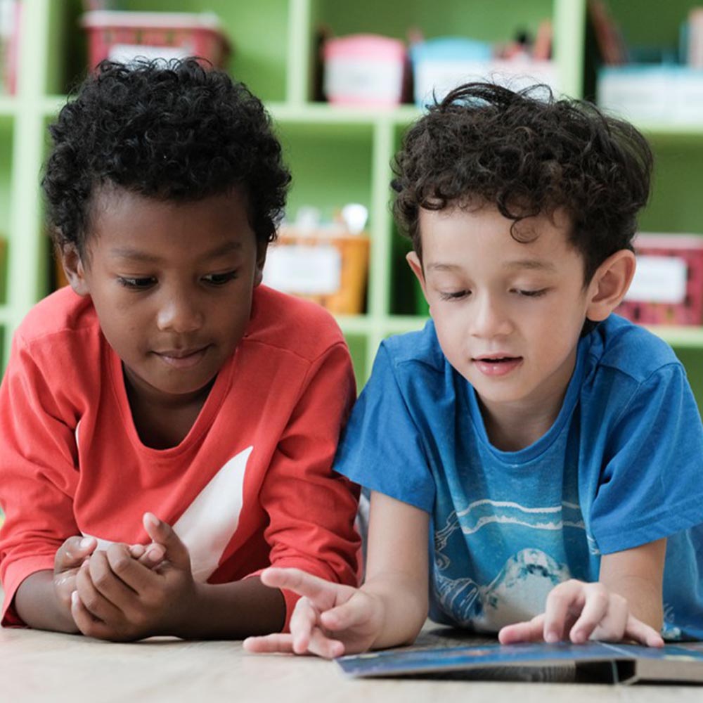 two boys laying on the ground reading a book